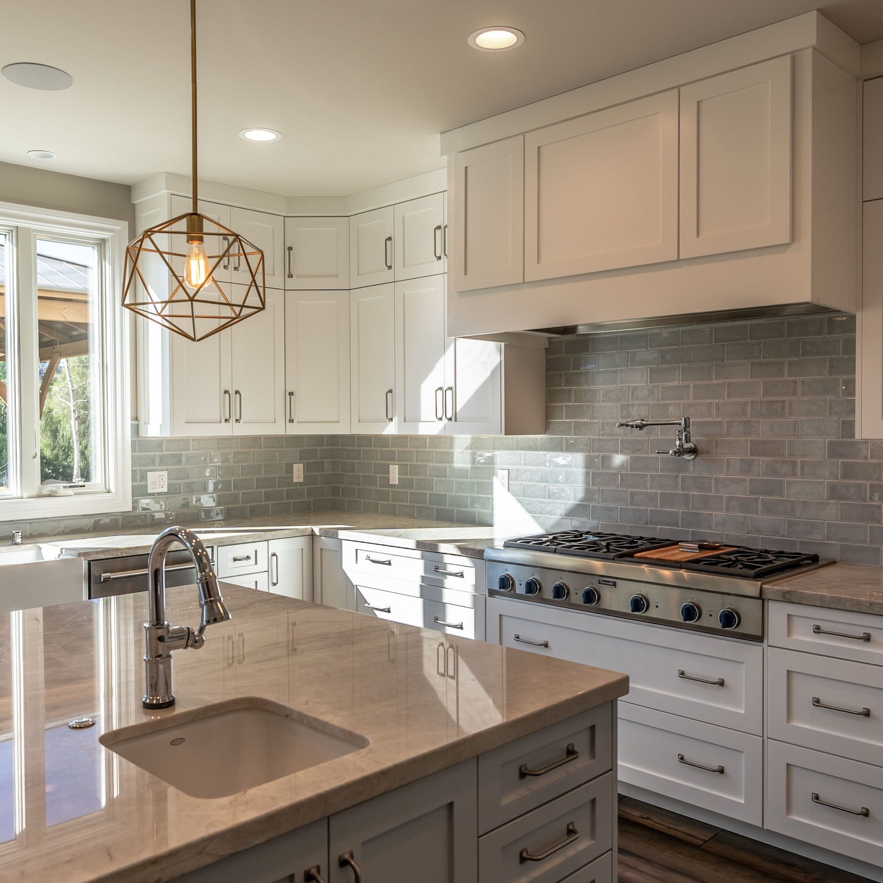 Kitchen detail from the Laguna Hills remodel. Include adjacent cabinetry and finishes in your project photos. White kitchen cabinets, a range, island sink and a window in the Laguna Hills kitchen.