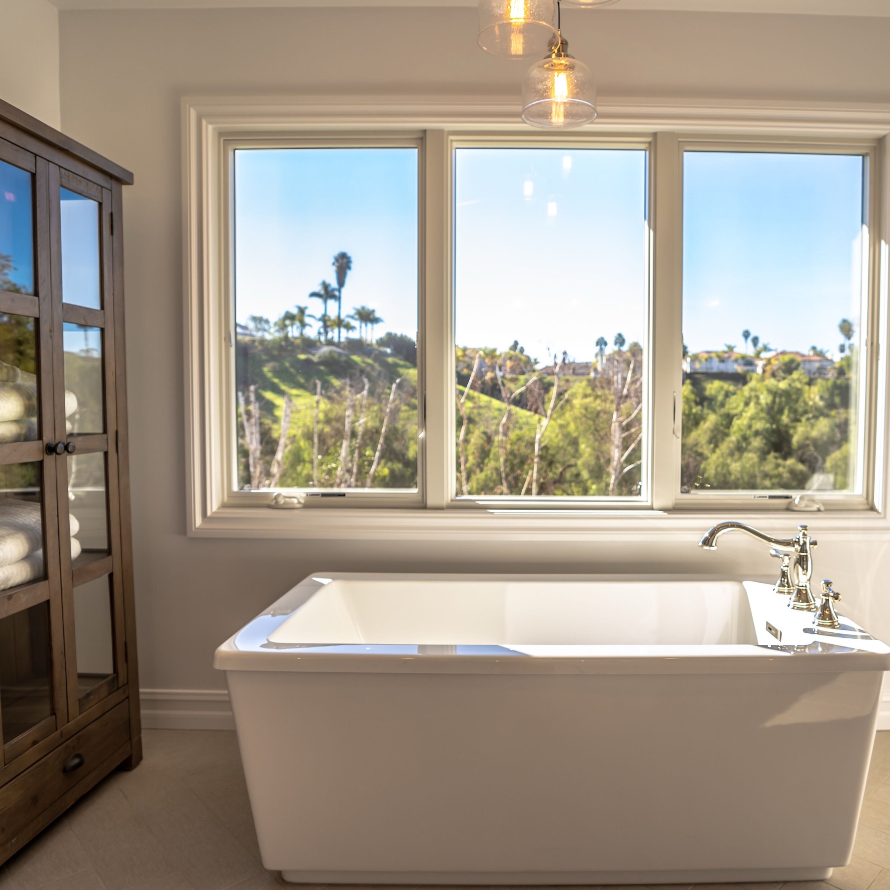 Laguna Hills: the window, tub and surrounding finishes belong in the same planning conversation. A white freestanding bathtub below a wide window in the Laguna Hills bathroom.